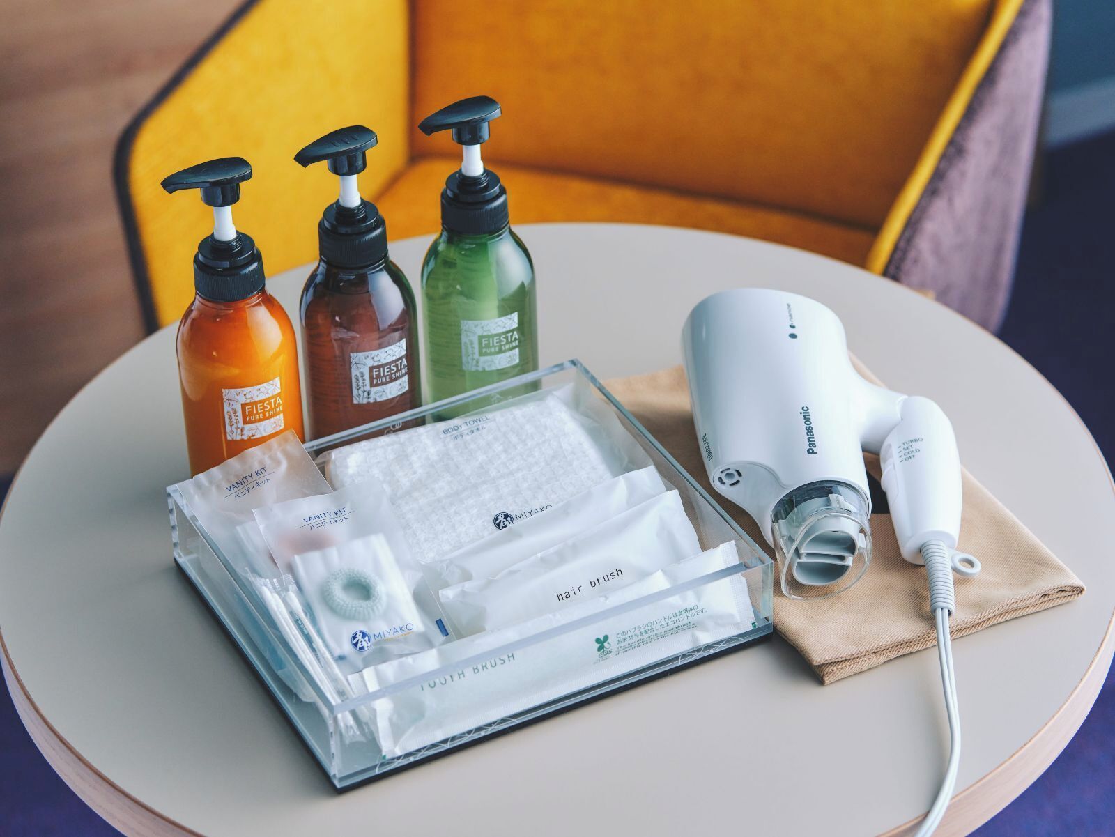 Un kit de tocador con un secador de pelo y tres botellas de productos para el cuidado corporal sobre una mesa.
