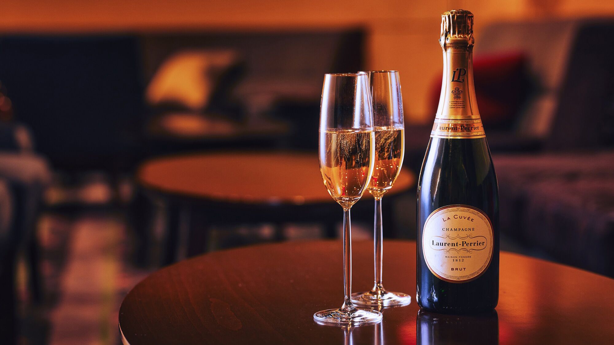 A bottle of champagne and two glasses on a table in a dimly lit room.