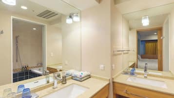 A hotel bathroom with two sinks, a shower, and a mirror.