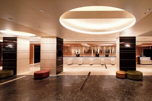 A modern lobby with a central reception desk, seating areas, and a large circular light fixture.