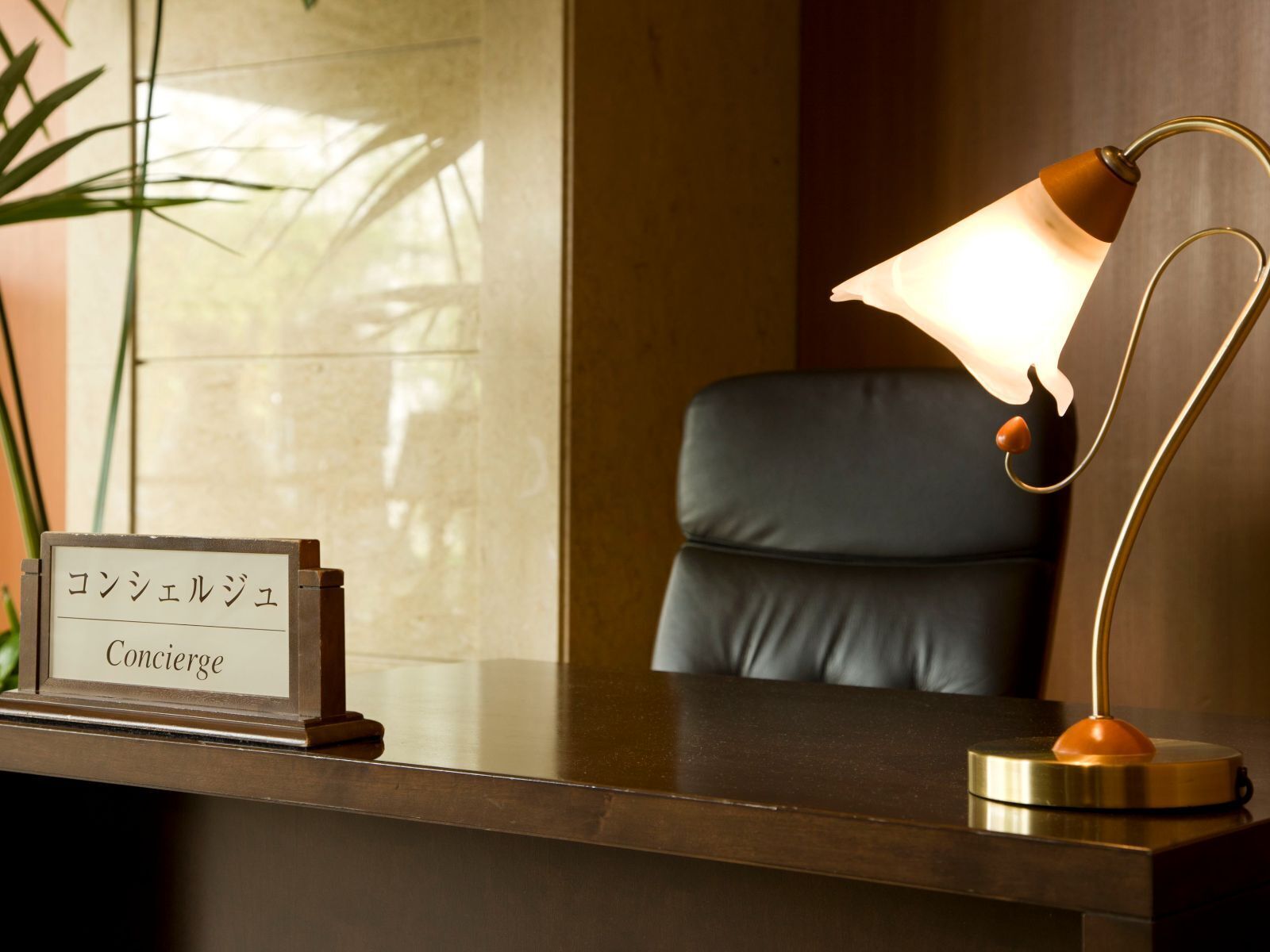 A reception desk with a sign reading "Concierge" in English and Japanese, a leather chair, and a desk lamp.