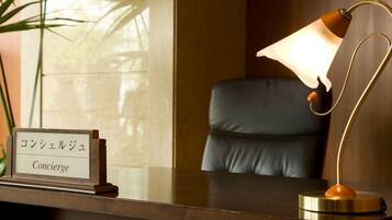 A reception desk with a sign reading "Concierge" in English and Japanese, a leather chair, and a desk lamp.