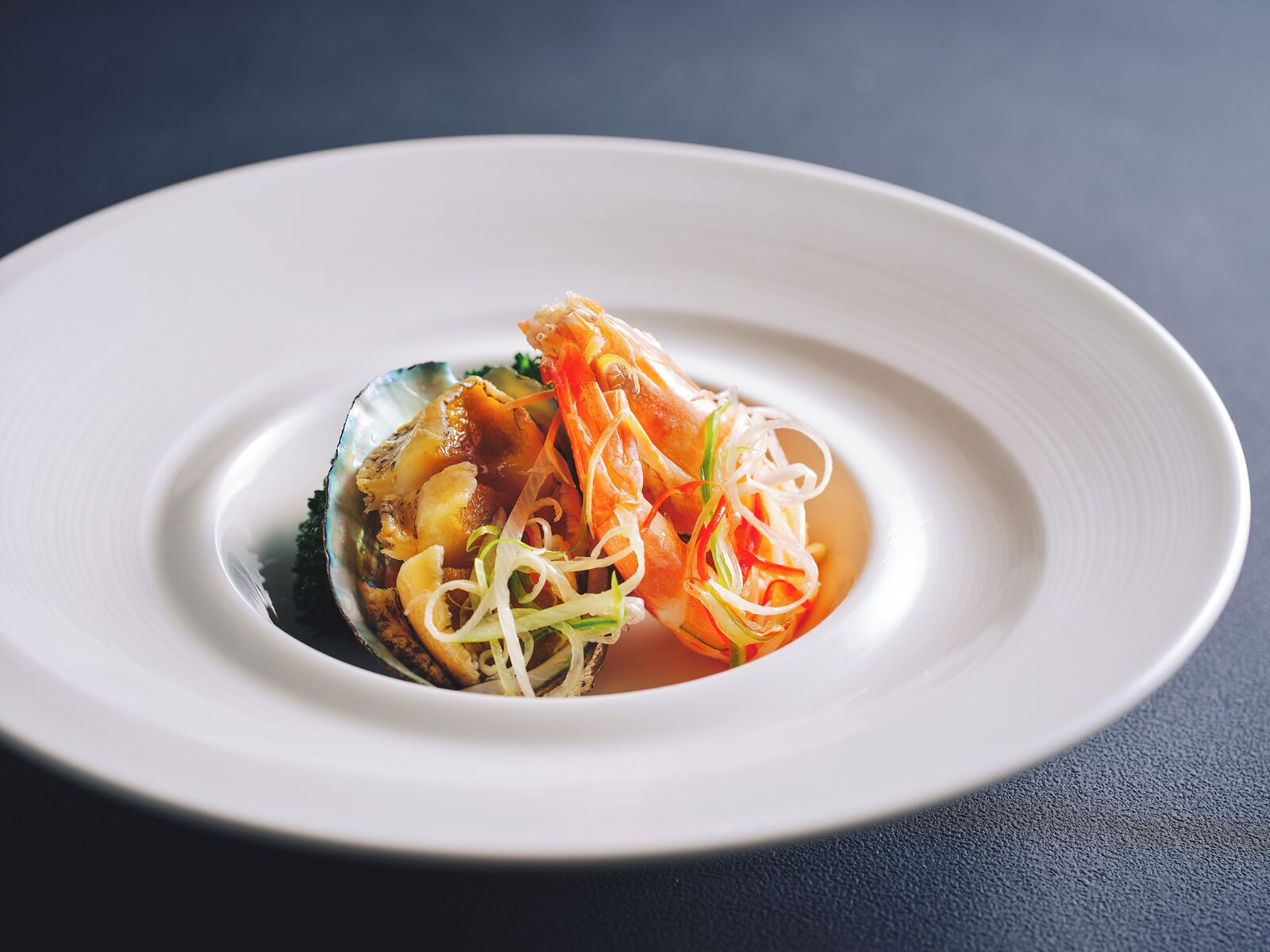 A plate with a seafood dish, possibly a clam or mussel, topped with shredded vegetables and a sauce.