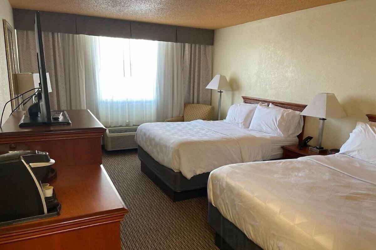 A hotel room with two beds, a desk, a chair, a TV, and a window with curtains.