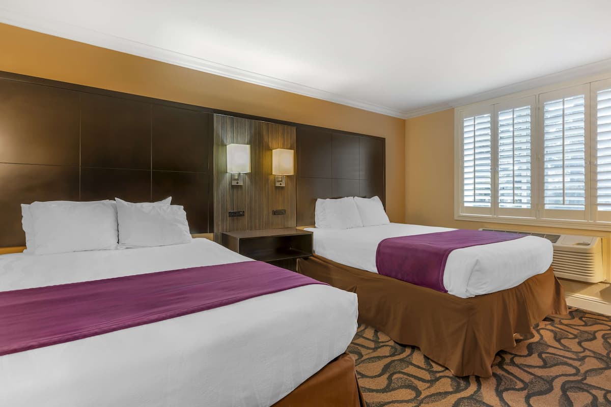 Hotelkamer met twee bedden, een groot hoofdeinde, een nachtkastje en een raam met jaloezieën.