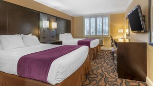 A hotel room with two beds, a desk, a TV, and a window with blinds.
