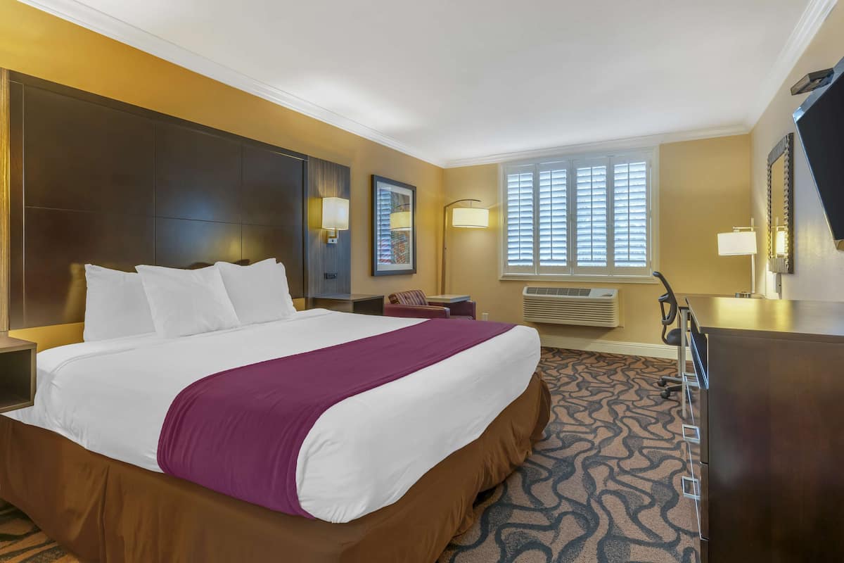 Hotelkamer met een groot bed, een bureau, een stoel, een dressoir en een raam met jaloezieën.