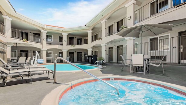 Un área de piscina con sillas de descanso y un jacuzzi, rodeada por un edificio de varios niveles con balcones.