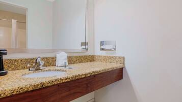 A bathroom with a granite countertop, two sinks, a mirror, and a towel dispenser.