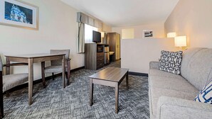 Habitación de hotel con una mesa de comedor, dos sillas, un sofá, un televisor, un armario y una alfombra estampada.