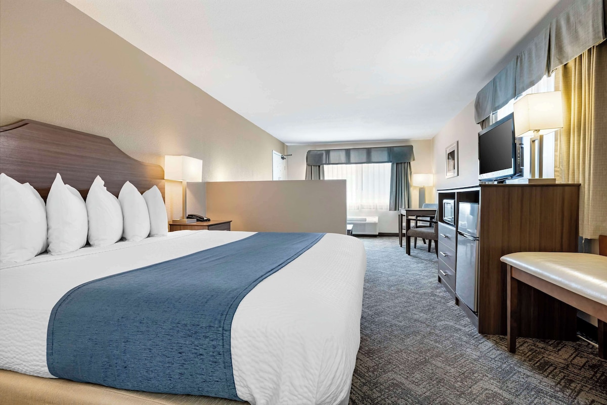 A hotel room with a large bed, a desk, a television, and a seating area.