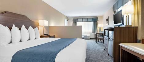 A hotel room with a large bed, a desk, a television, and a seating area.
