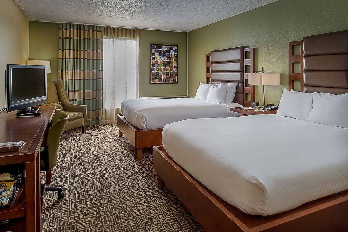 A hotel room with two beds, a desk with a television, a chair, and a patterned carpet.