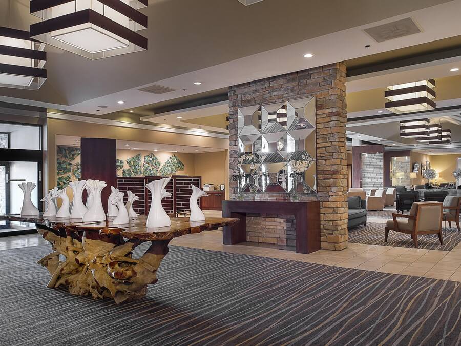 Un hall con una mesa central que exhibe jarrones, una pared de piedra con espejos y una zona de estar con sofás y sillones.