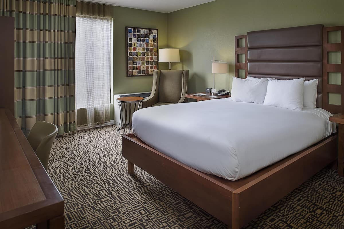 A hotel room with a large bed, a desk, a chair, a lamp, and a wall art piece.