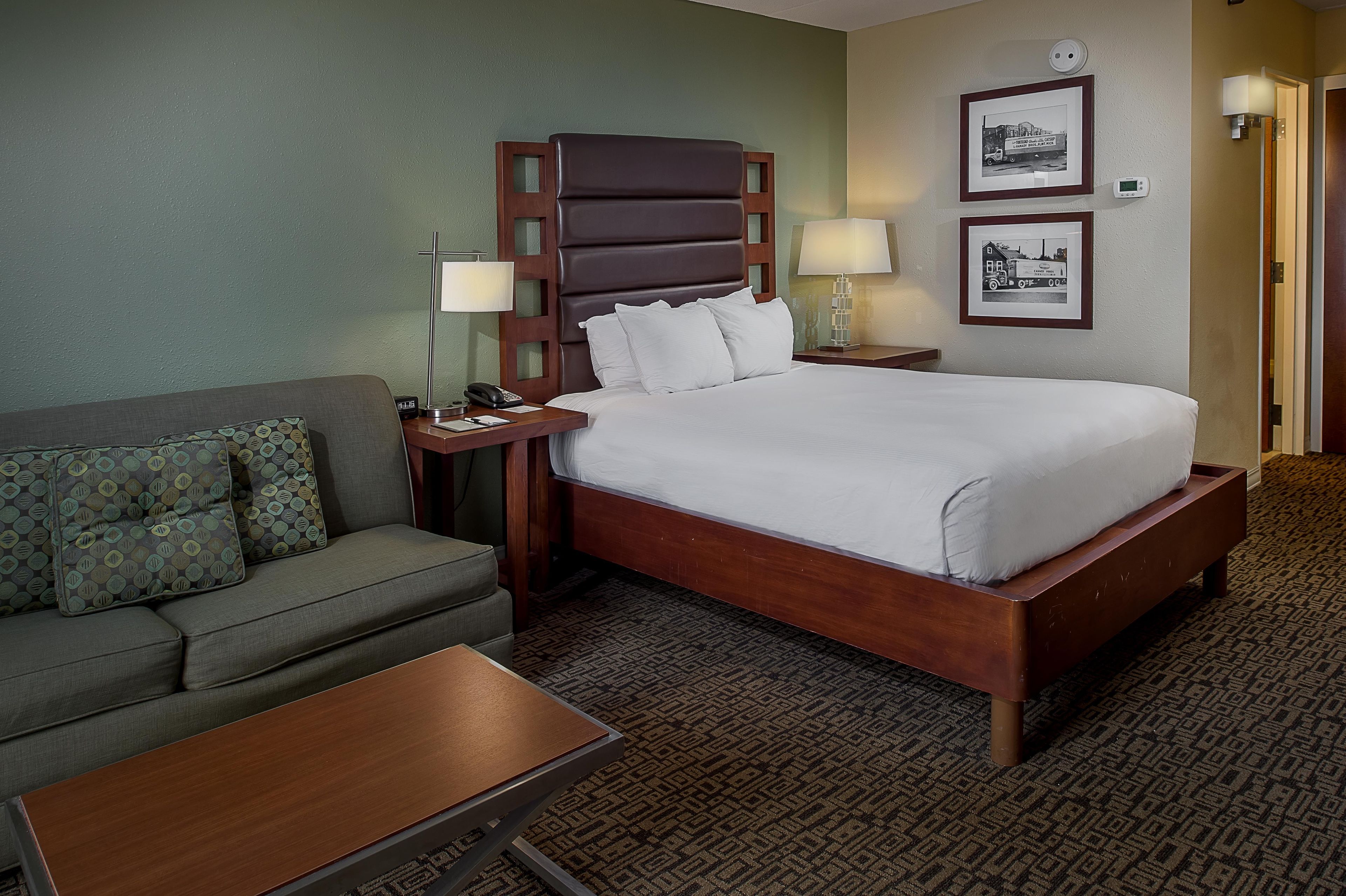 Una habitación de hotel con una cama, un sofá, una mesita de noche, una lámpara y un reloj.