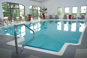 An indoor swimming pool with clear water, surrounded by lounge chairs and potted plants. - DoubleTree by Hilton Collinsville - St. Louis (Collinsville)