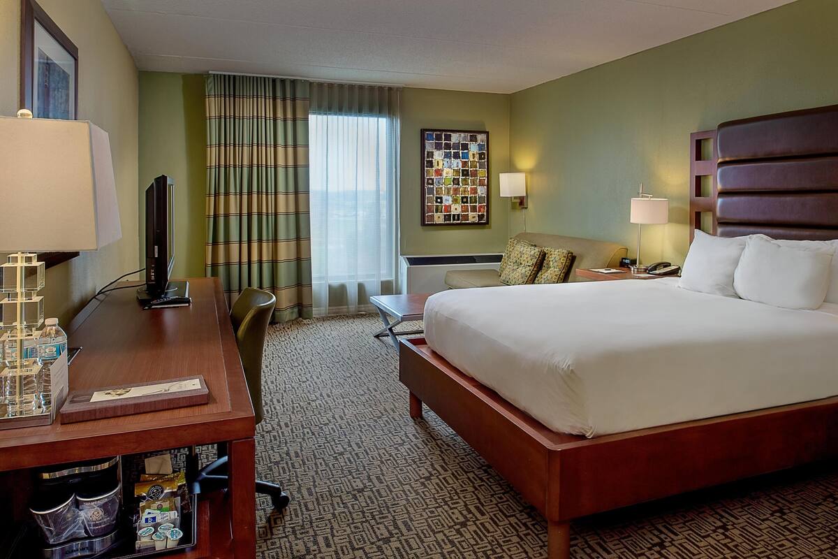 A hotel room with a bed, desk, chair, and a window with curtains.