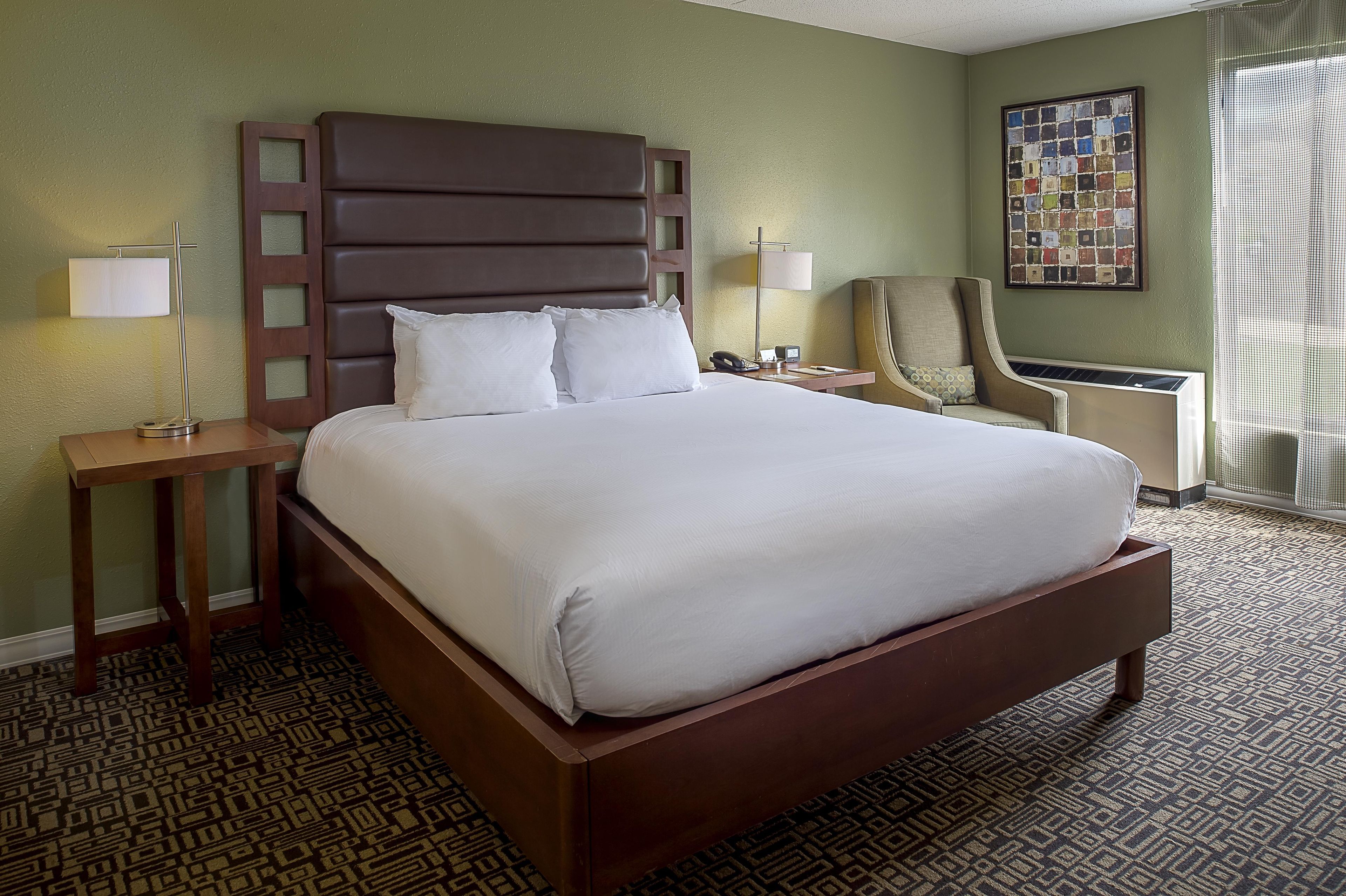 A hotel room with a large bed, two bedside tables, a chair, a desk, and a window with curtains.