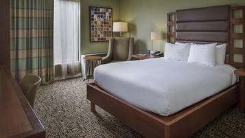 Een hotelkamer met een groot bed, een bureau, een stoel, een lamp en een kunstwerk aan de muur.