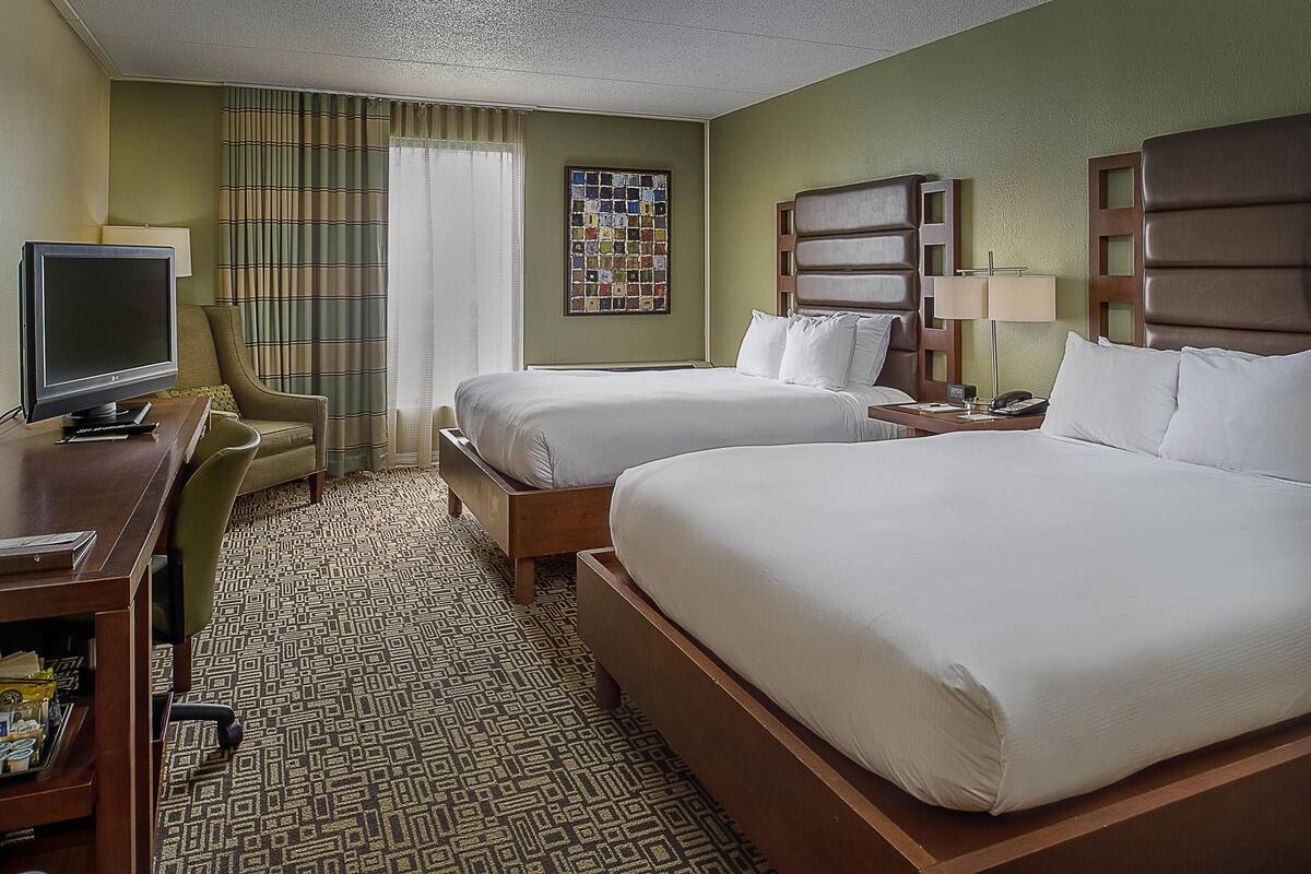 A hotel room with two beds, a desk with a computer, a chair, and a television.