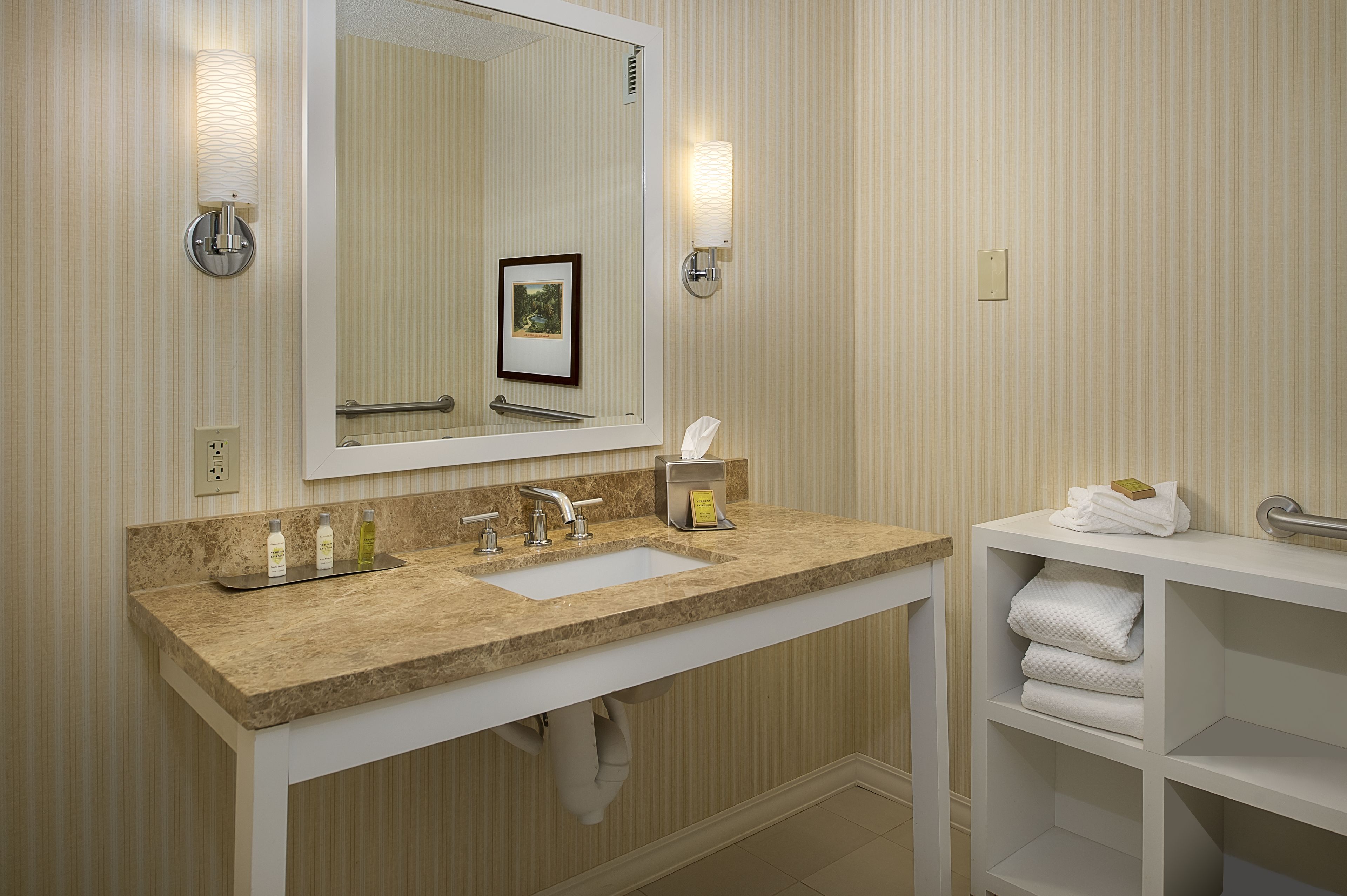 A bathroom with a marble sink, a large mirror, a towel rack, and a shelf with folded towels.