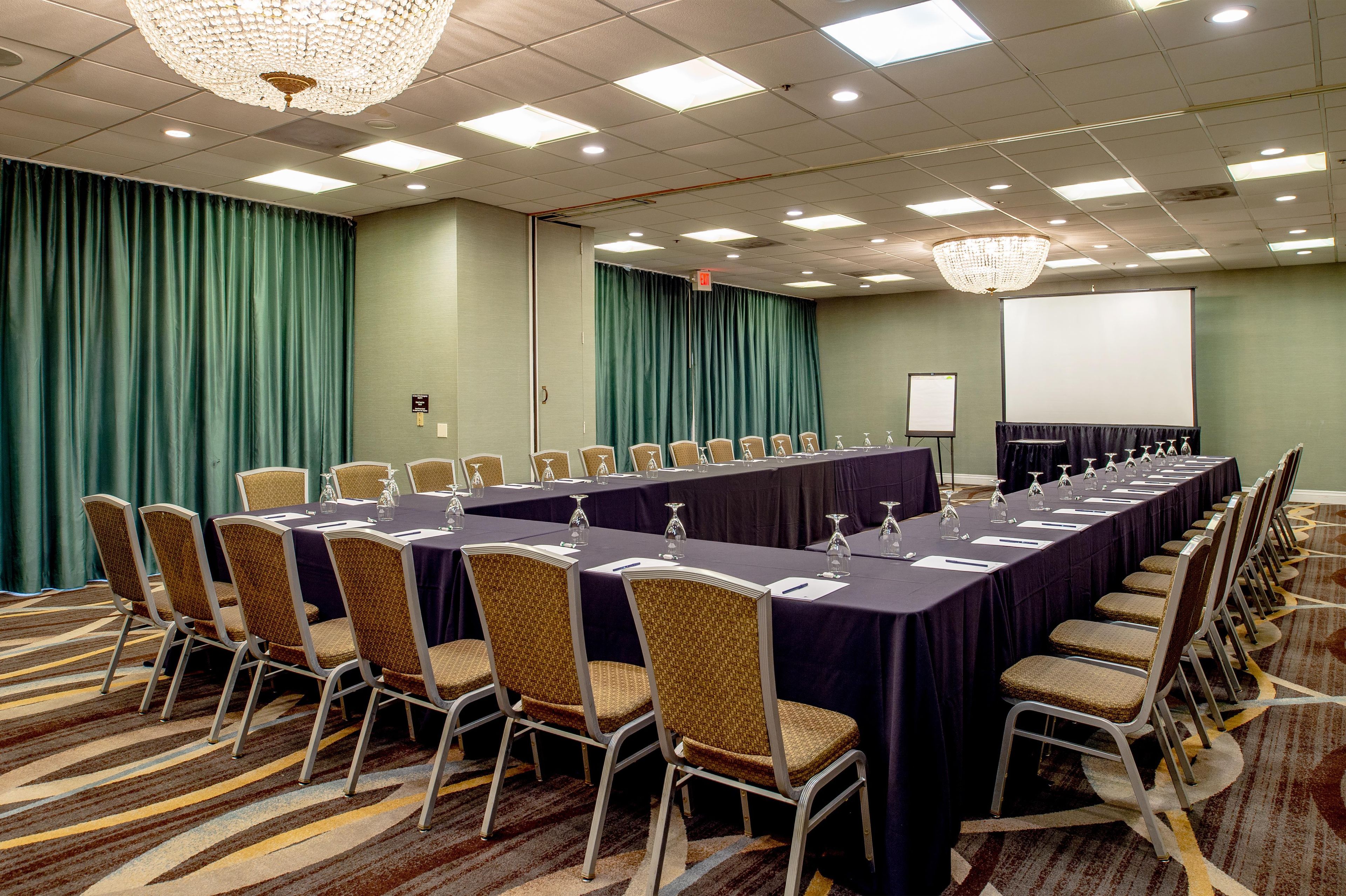 A conference room with a long table, chairs, a projector screen, and a chandelier.