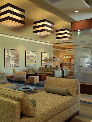 A modern hotel lobby with a sectional sofa, armchairs, a coffee table, and abstract wall art. - DoubleTree by Hilton Collinsville - St. Louis (Collinsville)
