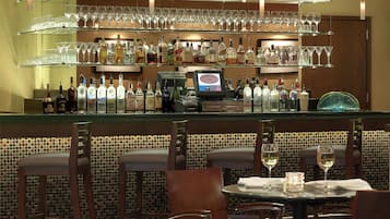 A bar area with multiple shelves of bottles and glasses, a cash register, and seating with tables and chairs.