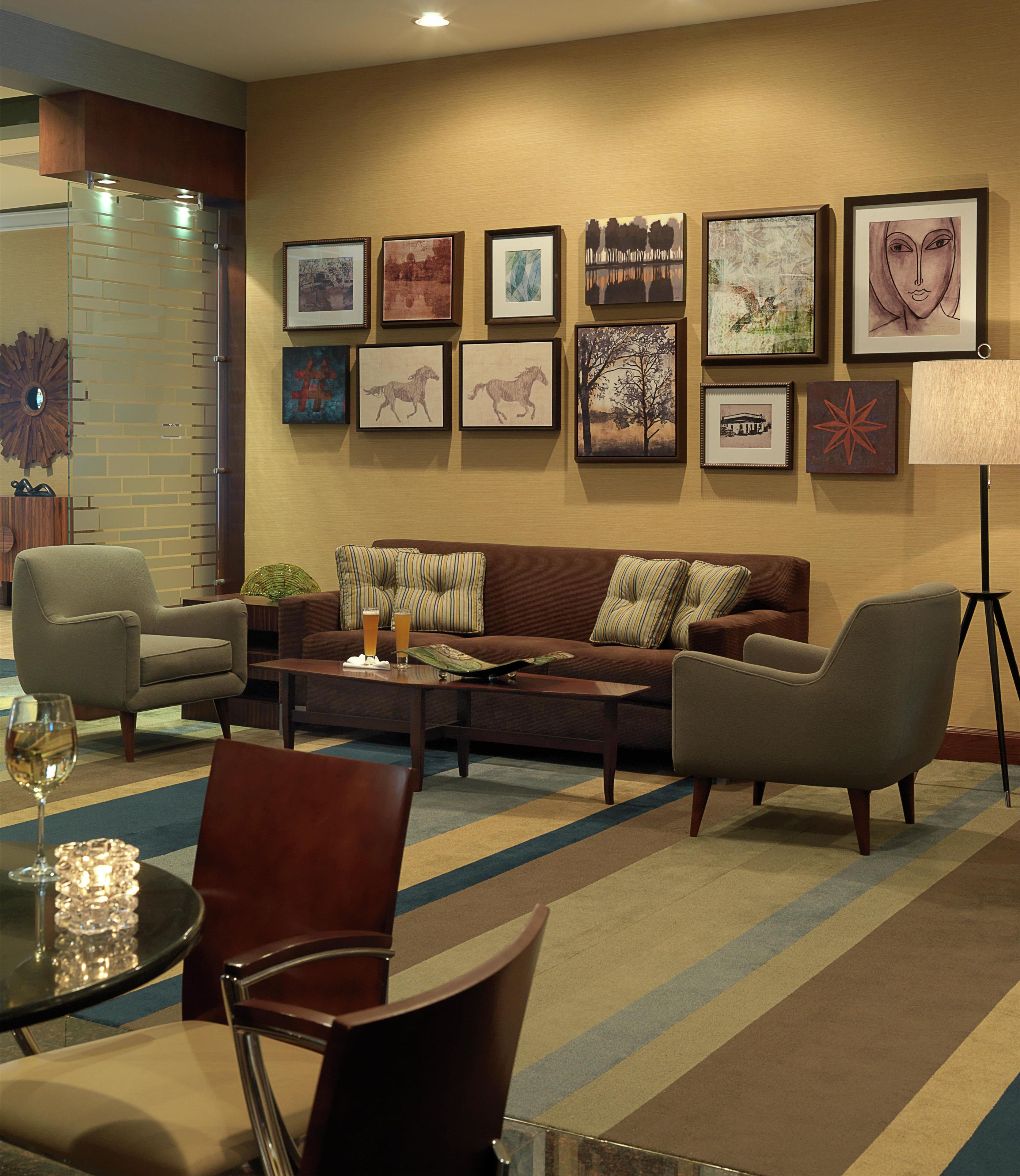A hotel room with a sofa, armchairs, a coffee table, and a dining table with a glass of wine.