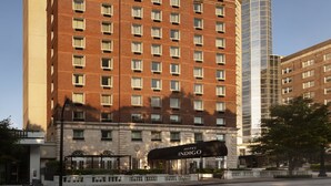 Un hotel de varios pisos con fachada de ladrillo clásico, un llamativo letrero de 'Hotel Indigo' y una torre de cristal moderna adyacente.