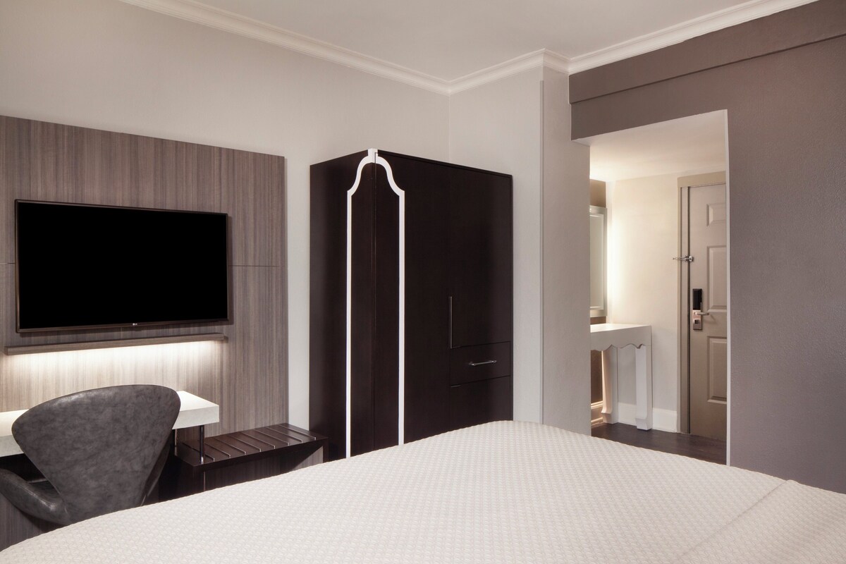 Una camera d'albergo con un letto, una scrivania con sedia, una TV a parete e un armadio.