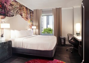 Une chambre d’hôtel avec un grand lit, un bureau, une chaise, une lampe et une vue sur un immeuble par la fenêtre.