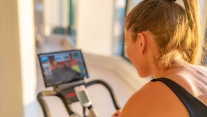 Una persona usando una bicicleta estática con pantalla digital, en una habitación con ventana y puerta.
