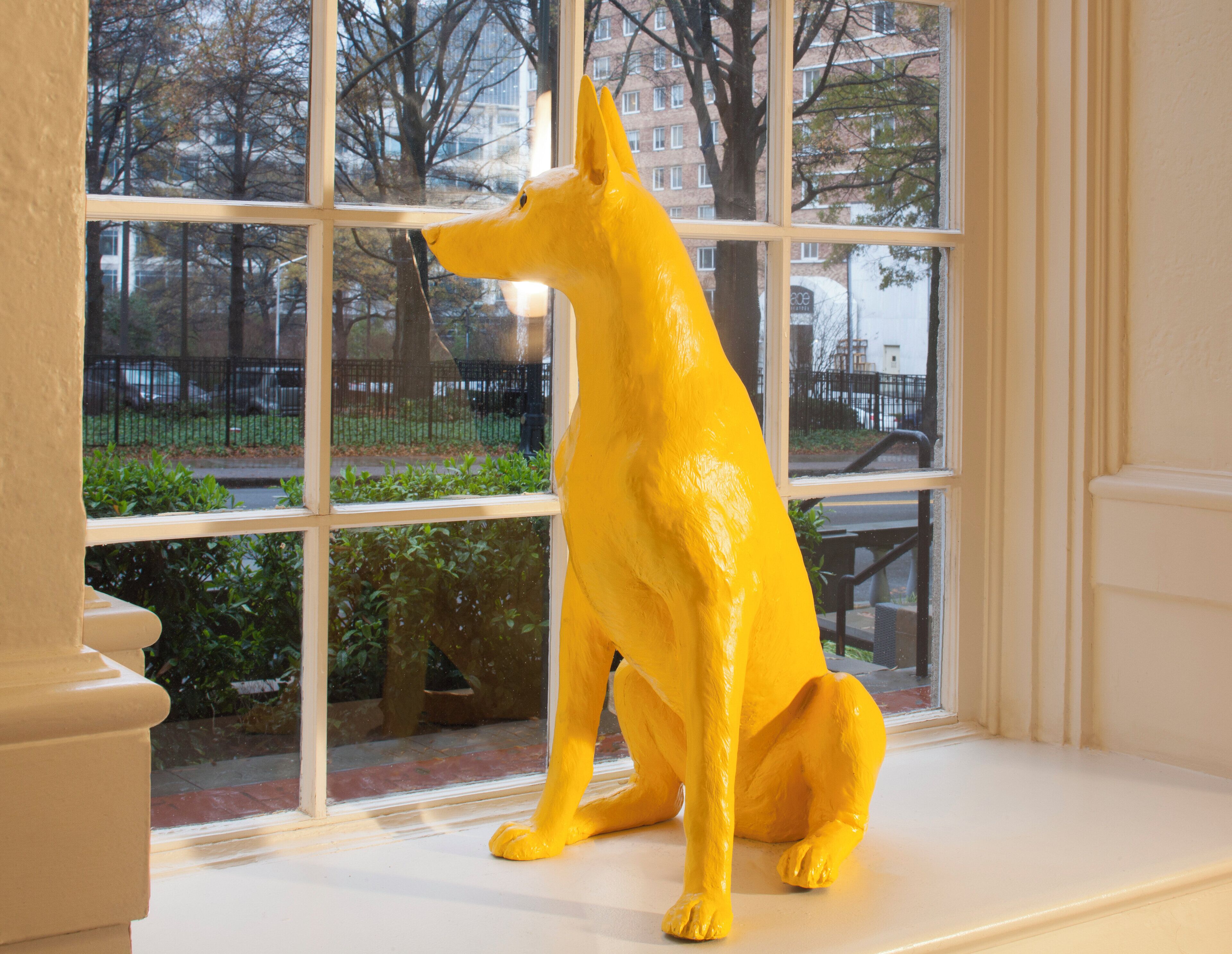 A bright yellow sculpture of a dog sitting on a window sill.