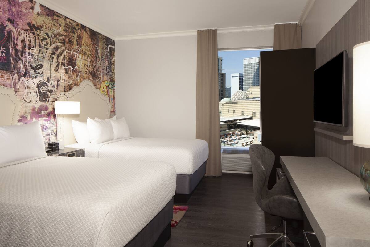 Una habitación de hotel con dos camas, un escritorio, un televisor y un ventanal con vista a la ciudad.