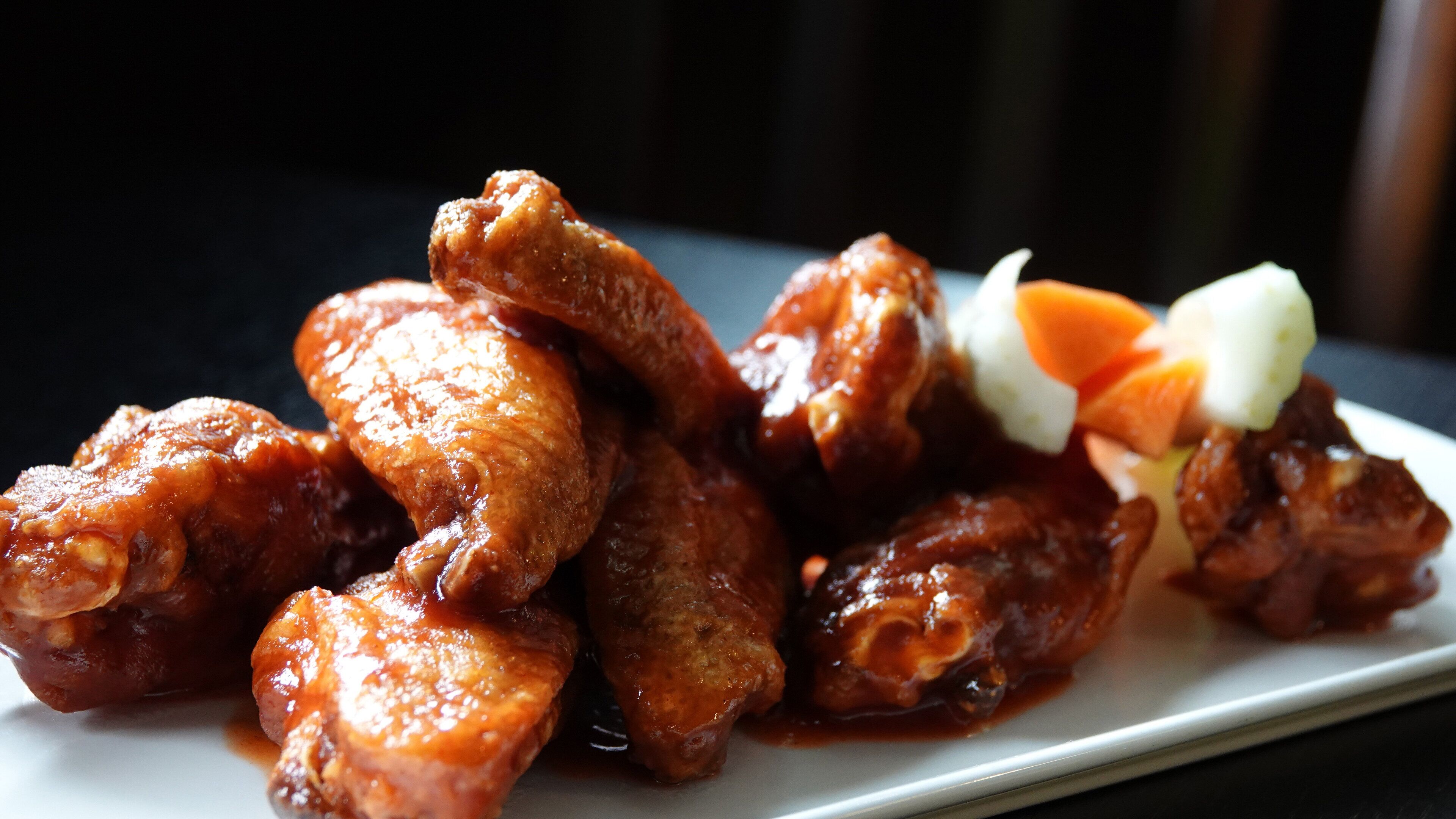 A plate of glazed chicken wings with carrot sticks and a white sauce.