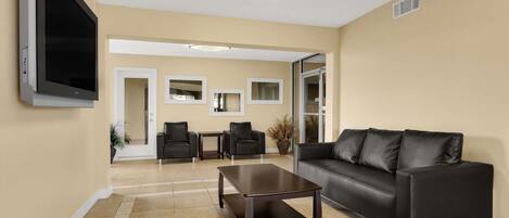 A modern living room with a black leather sofa, a wooden coffee table, and a flat-screen TV mounted on the wall.
