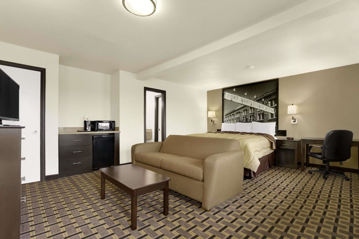 Une chambre d’hôtel comprenant un lit, un canapé, un bureau, une chaise, une petite table et un coin cuisine avec un four à micro-ondes, ainsi qu’un sol à motifs.