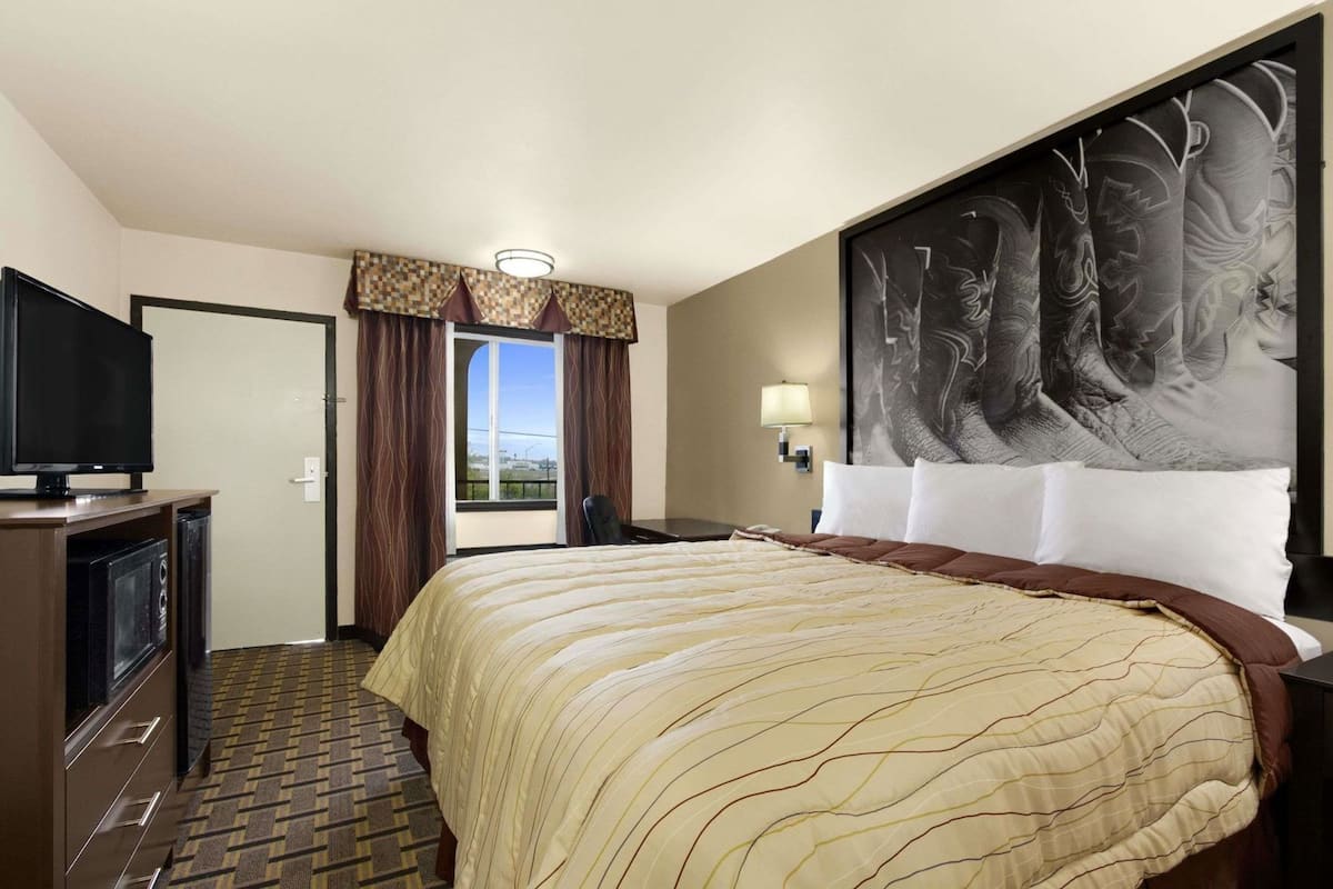 Une chambre d’hôtel équipée d’un lit, d’une télévision, d’un bureau, d’une chaise, d’une fenêtre avec des rideaux et d’une lampe fixée au mur.