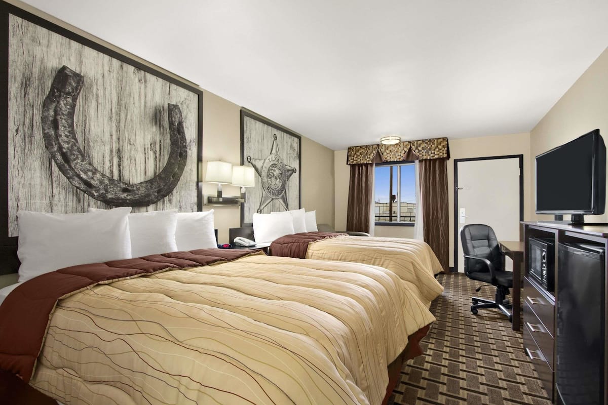 Une chambre d’hôtel avec deux lits, un bureau avec un ordinateur, une télévision et une vue sur l’extérieur.