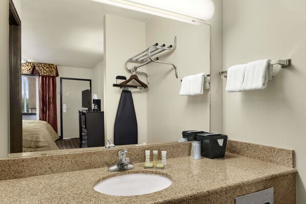 Une salle de bain d’hôtel avec un comptoir en granit, un lavabo, un miroir, un porte-serviettes et une pomme de douche suspendue.