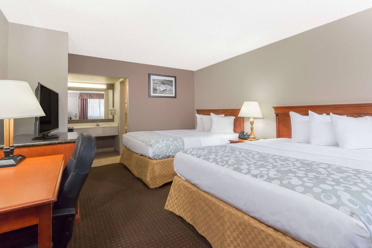 A hotel room with two beds, a desk with a chair, a television, and a mirror.