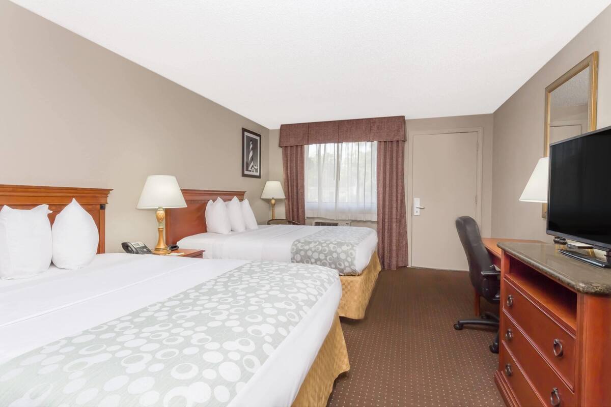 A hotel room with two beds, a desk, a chair, a television, and a window with curtains.