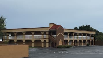 A large, multi-story building with a central staircase, multiple balconies, and a parking lot in front.