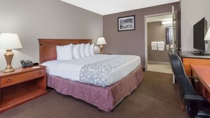 A hotel room with a bed, bedside lamps, a desk with a chair, a television, and a bathroom visible through an open door. - Days Inn by Wyndham St Augustine/Historic Downtown (St. Augustine)