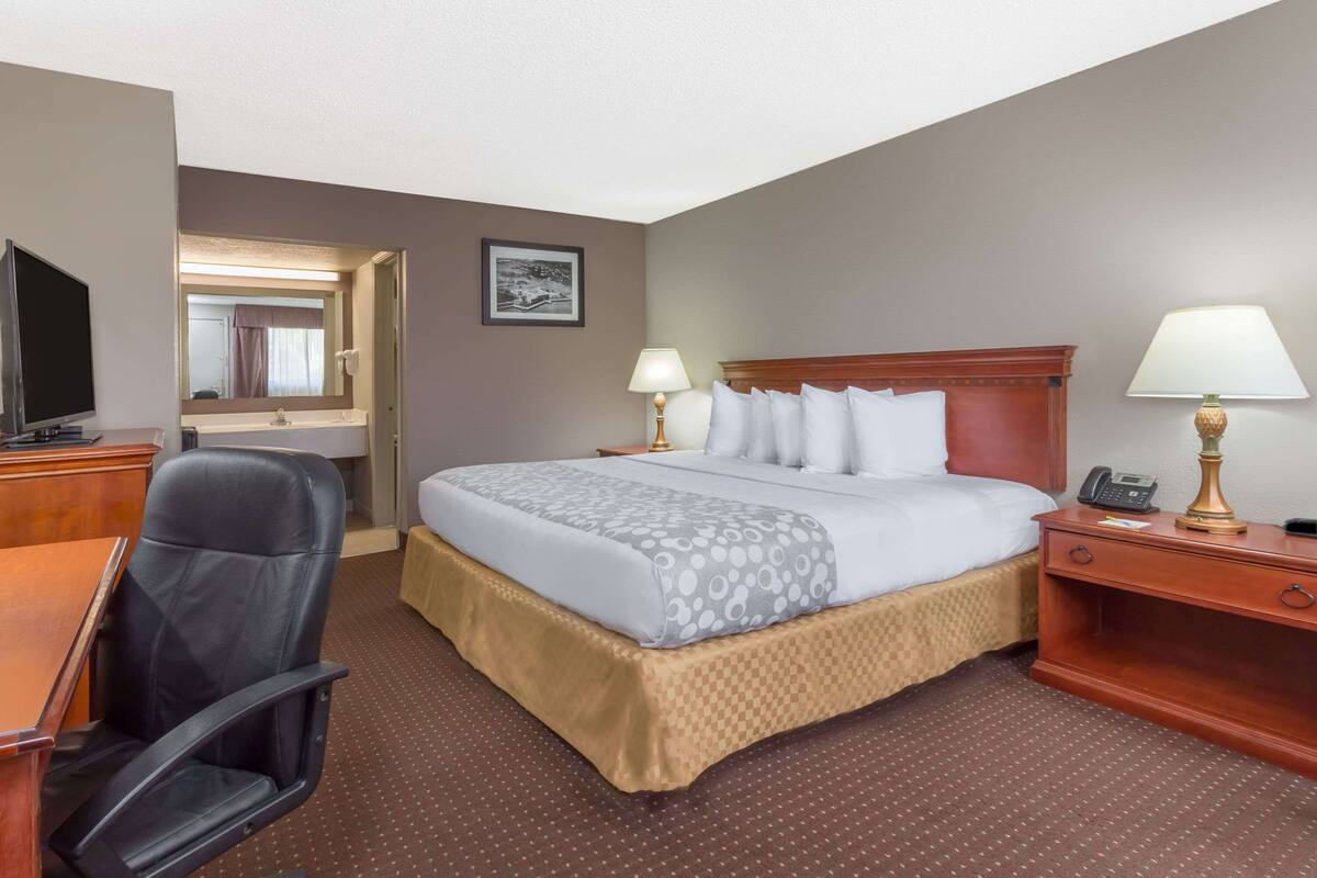 A hotel room with a bed, a desk with a chair, a television, and a lamp.