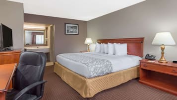 Una habitación de hotel con cama, escritorio, silla, televisor y lámpara.