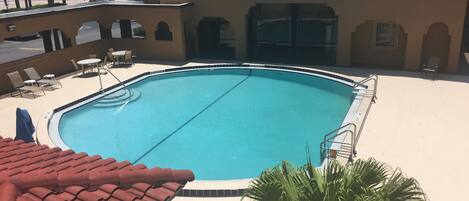 A swimming pool with a tiled deck, palm trees, and a building with arched doorways.