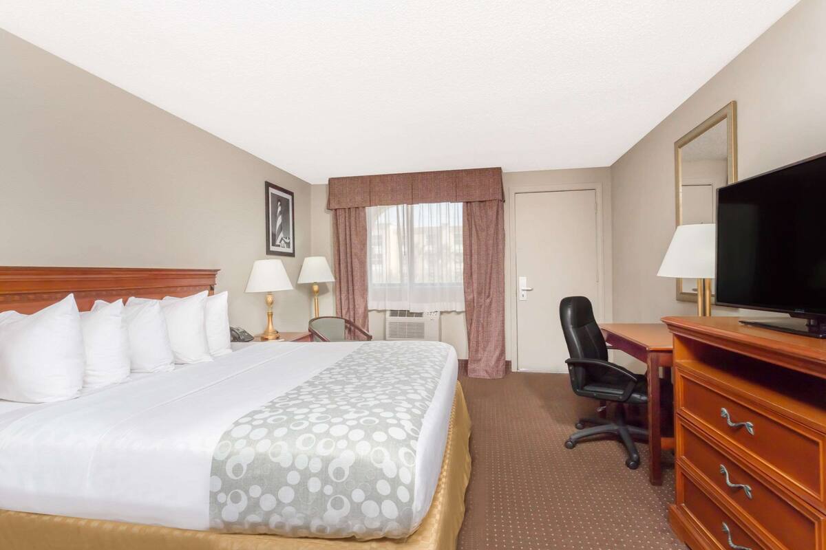 A hotel room with a large bed, a desk with a television, a chair, and a window with curtains.